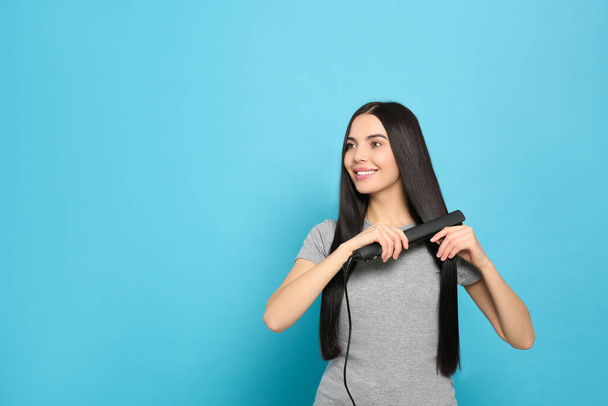 Beautiful happy woman using hair iron on light blue background. Space for text - Fotó, kép