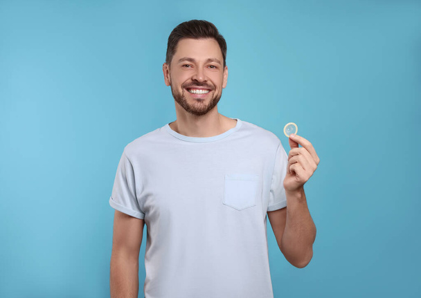 Happy man holding condom on light blue background - Фото, изображение