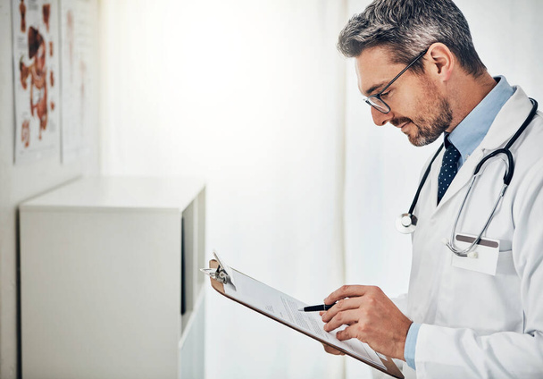 Перевірка прогресу пацієнтів. зосереджений лікар читає пацієнтський файл, стоячи у своїй консультаційній кімнаті
 - Фото, зображення