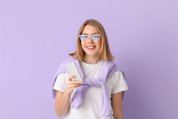 Young woman in eyeglasses using mobile phone on lilac background - Foto, Imagem