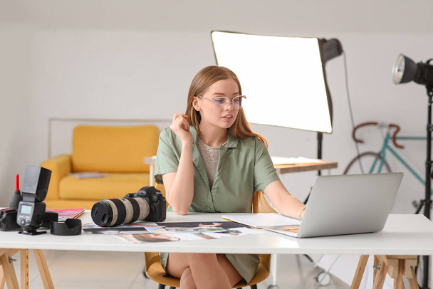 Νεαρή γυναίκα φωτογράφος που εργάζεται με φορητό υπολογιστή στο τραπέζι στο στούντιο - Φωτογραφία, εικόνα