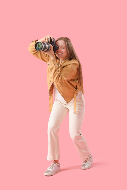 Νεαρή γυναίκα φωτογράφος με επαγγελματική κάμερα σε ροζ φόντο - Φωτογραφία, εικόνα