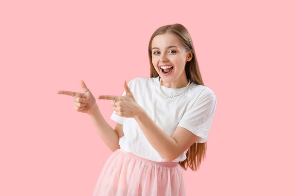 Happy young woman in t-shirt pointing at something on pink background - Zdjęcie, obraz