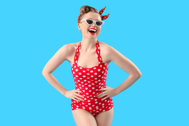 Young pin-up woman in polka dot swimsuit on blue background - Фото, зображення