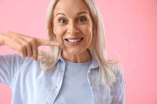 Kypsä nainen osoittaa hampaitaan vaaleanpunaisella taustalla, lähikuva - Valokuva, kuva