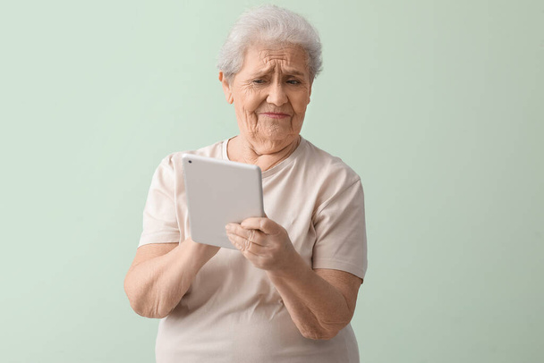 Donna anziana scontenta con tablet computer su sfondo verde - Foto, immagini