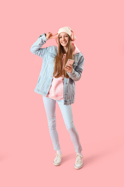 Female student with headphones and mobile phone on pink background - Foto, afbeelding