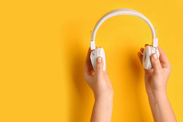 Woman holding modern white headphones on yellow background - Foto, afbeelding