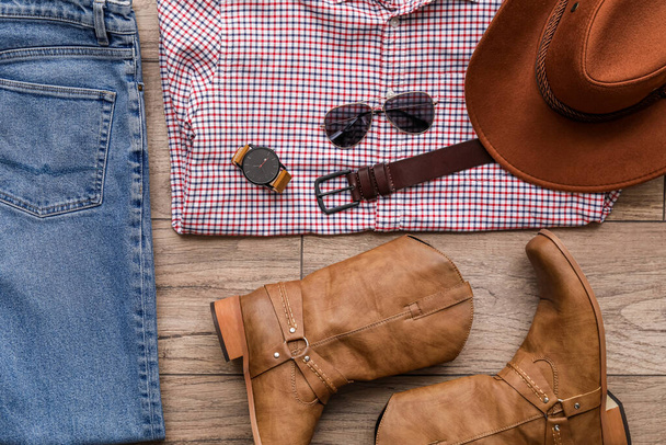 Male clothes with cowboy boots and accessories on wooden floor - 写真・画像