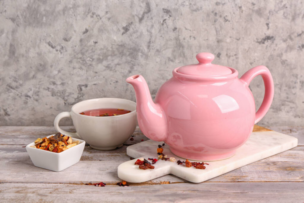 Deska z ceramicznym czajniczek i filiżanka herbaty owocowej na drewnianym stole w pobliżu ściany grunge - Zdjęcie, obraz