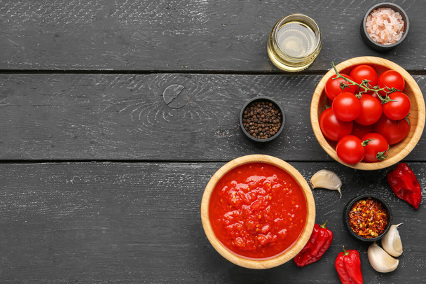 Ciotole con gustosa salsa di pomodoro e ingredienti su sfondo di legno scuro - Foto, immagini