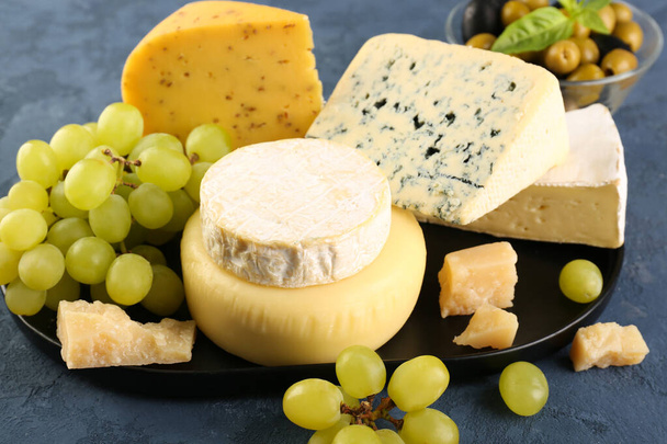 Plate with different types of cheese and grapes on blue background - Photo, Image