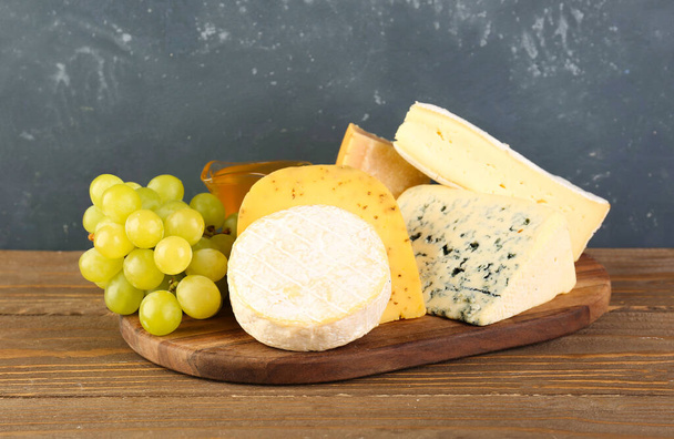 Wooden board with different types of cheese and grapes on table - Фото, зображення