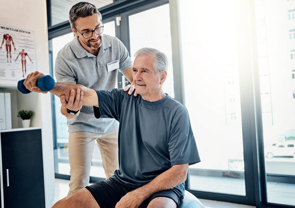 Wellness erfordert ein wenig Arbeit. ein freundlicher Physiotherapeut hilft seinem mündigen Patienten, in einem Reha-Zentrum Hanteln zu benutzen - Foto, Bild