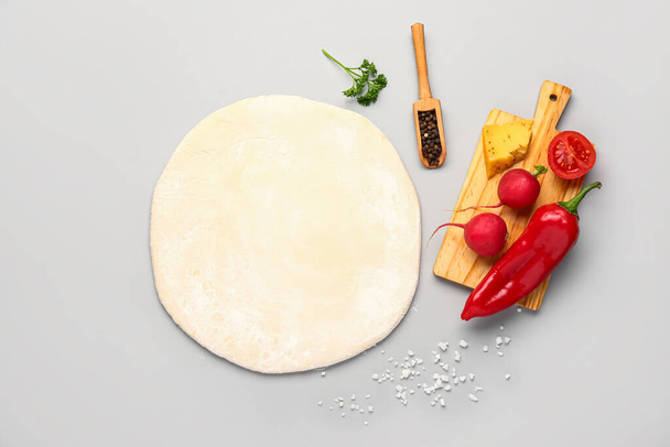 Raw dough and board with ingredients for preparing vegetable pie on grey background - Foto, afbeelding