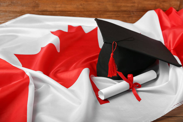 Sombrero de graduación con diploma y bandera de Canadá sobre fondo de madera, primer plano - Foto, imagen