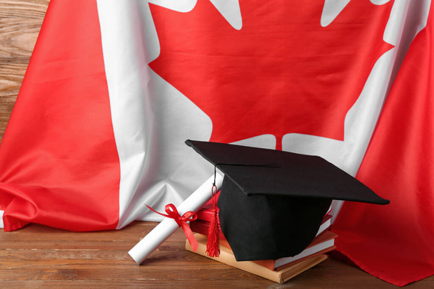 Καπέλο αποφοίτησης με δίπλωμα, βιβλία και σημαία Καναδά σε ξύλινο τραπέζι - Φωτογραφία, εικόνα