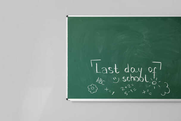 Blackboard with text LAST DAY OF SCHOOL and drawings on white wall - Photo, Image