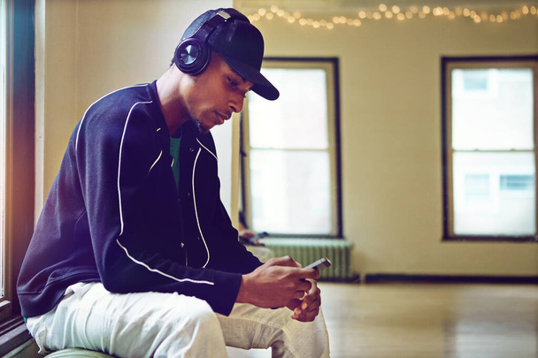 Listening to the dopest beats. a young man using his phone and headphones in a dance studio - Foto, imagen
