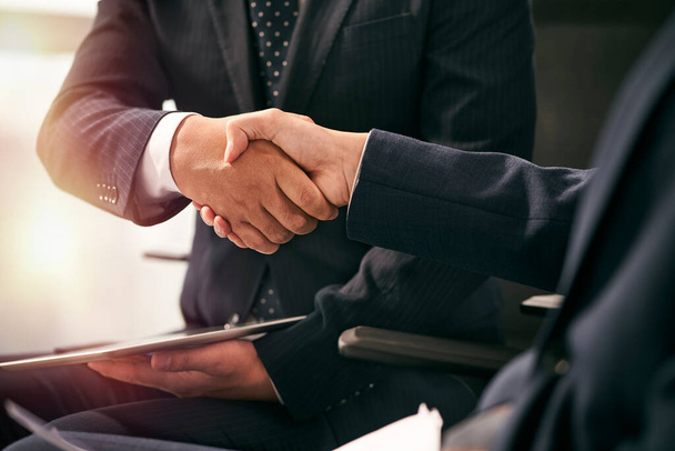 plan rapproché de deux hommes d'affaires asiatiques partenaires coéquipiers assis dans des chaises serrant la main dans le bureau - Photo, image