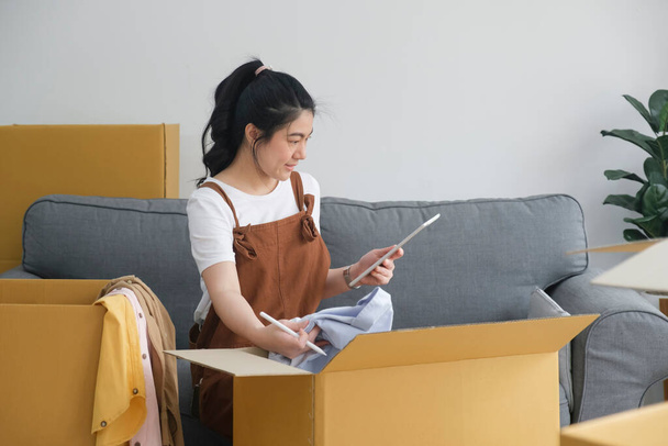 Ázsiai nő ellenőrzése és csomagolása a kartondoboz felkészülni költözni az új ház áthelyezése szállítási vagy ellenőrizze áruk csomag szállítás előtt az ügyfél az online vásárlás által ellenőrzőlista - Fotó, kép