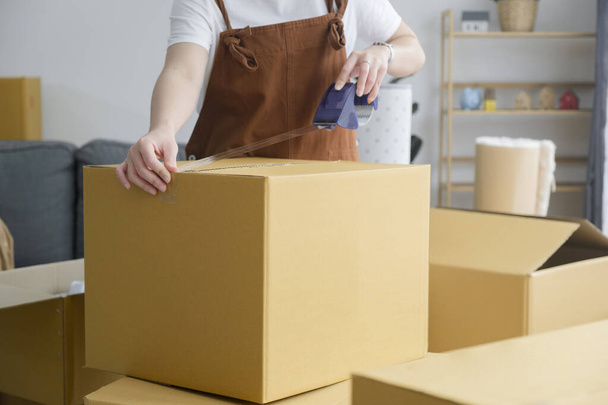 Happy single young woman packing stuff among plenty of cardboard boxes cardboard boxes while moving to new house. Living alone. Modern female people in moving home apartment leisure indoor activity - Photo, Image