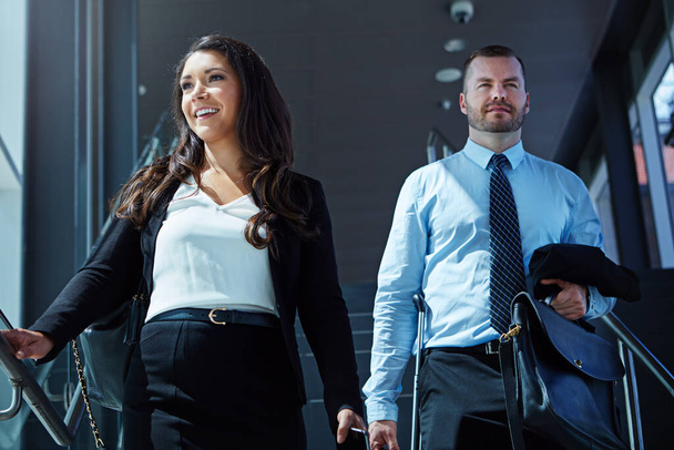 Профессионалы прибыли. бизнесмен и деловая женщина, спускающиеся по эскалатору в аэропорту - Фото, изображение