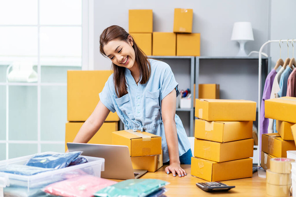 Portrait young attractive asia female owner startup business using computer laptops work happy with carton box at home prepare delivery to customers, procurement, omnichannel ecommerce online concept - Фото, изображение