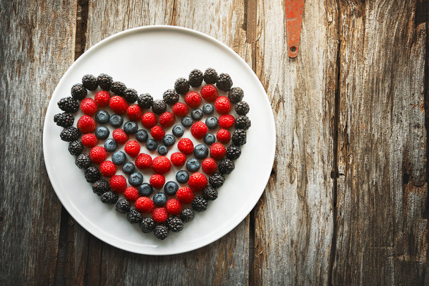 Ешь своё сердце. Высокоугольный выстрел ягод в форме сердца на тарелке - Фото, изображение
