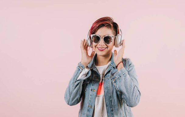 nuori latinonainen kuuntelee musiikkia kuulokkeilla ja pitää matkapuhelin koralli vaaleanpunainen tausta kopioi tilaa studio muotokuva Meksikossa Latinalaisessa Amerikassa, latinonainen - Valokuva, kuva