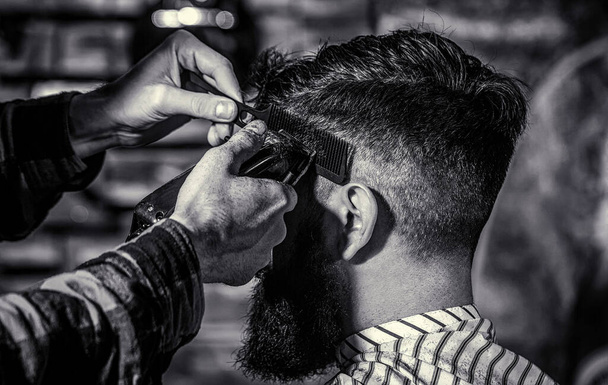 Concepto de corte de pelo. Hombre visitando peluquero en barbería. Peluquero trabaja con el cortador de pelo. Hipster cliente cortarse el pelo. Blanco y negro. - Foto, imagen