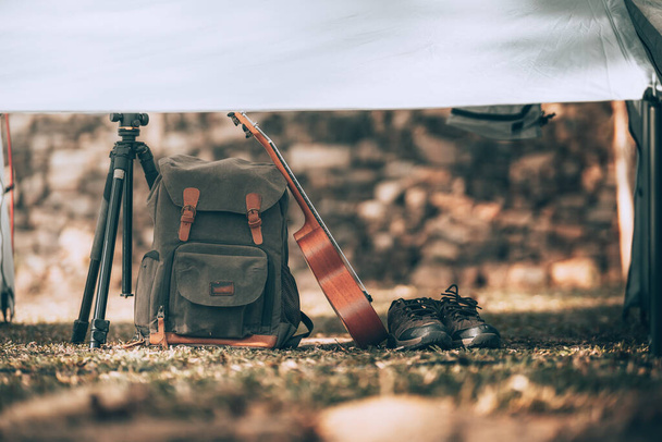 Camping equipment, bags, shoes, ukulele, tripod in tent in the morning. Object camp, Travel and vocation concept. - Photo, image