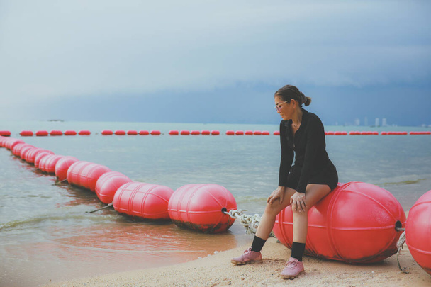 женщина в черном спортивном костюме сидит на плавучем барьере на морском пляже - Фото, изображение