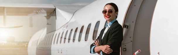 Woman flight attendant in sunglasses standing on airplane stairs at airport. Blurred background - Foto, Imagen