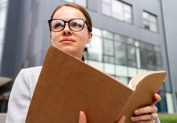 Портрет деловая женщина в очках держит папку с документацией в руках и смотрит в сторону. - Фото, изображение