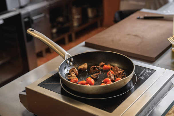 Tomatoes and mushrooms is cooking in frying pan in restaurant kitchen. High quality photo - Zdjęcie, obraz