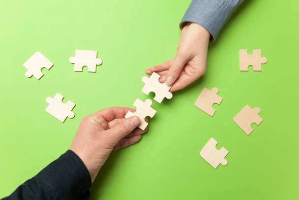 Two hands connect puzzles on a green background. Cooperation and teamwork in business. Collaboration people for success. - Foto, afbeelding