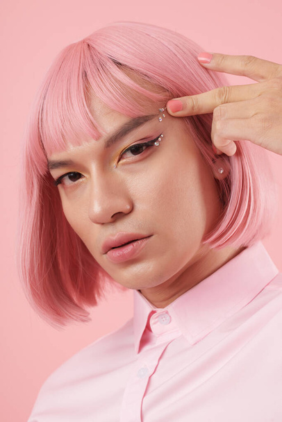Portrait of young man pulling off sparkling rhinestones makeup and pink wig - Photo, Image