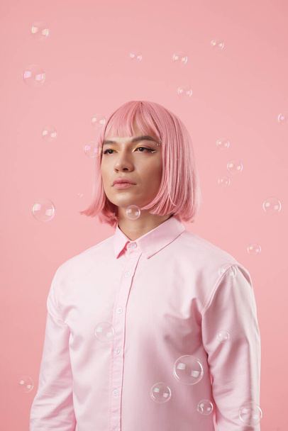 Retrato de un joven asiático con un hermoso aspecto ocular y un corte de pelo rosa bajo burbujas de jabón que caen - Foto, imagen