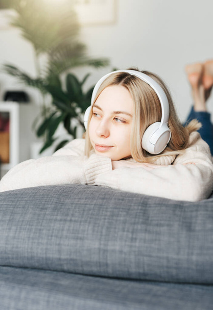 Young blonde woman in headphones listening to music and relaxing at home. - 写真・画像