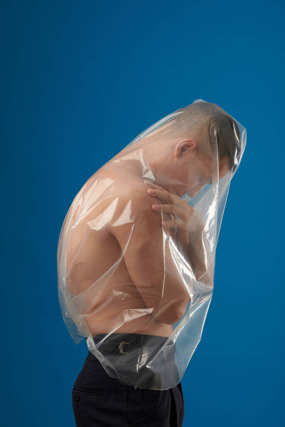 Hemdloser junger Mann in durchsichtiger Plastiktüte auf blauem Hintergrund - Foto, Bild