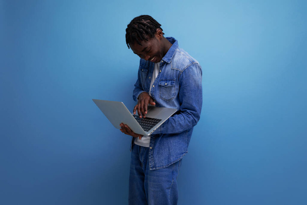 odnoszący sukcesy freelancer amerykański człowiek z dredami w dżinsowej kurtce działa zdalnie za pomocą laptopa. - Zdjęcie, obraz