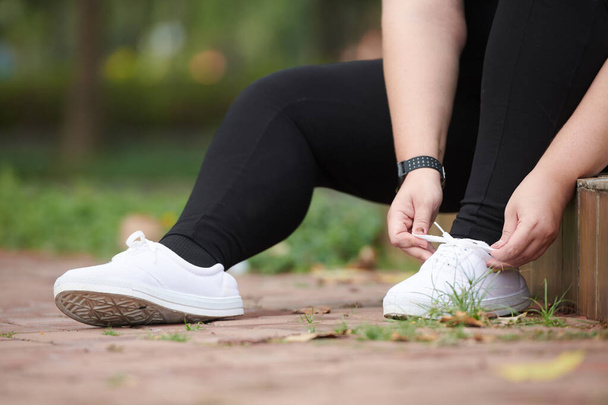 Плюс-размер молодая женщина завязывает шнурки для бега в парке утром - Фото, изображение