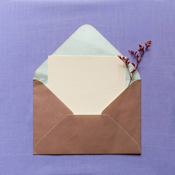 Flat lay composition with dry flowers and envelope mockup with blank greeting card on lilac background. Minimal floral frame. top view. Happy mother's day, women's day, birthday or wedding. - Photo, Image