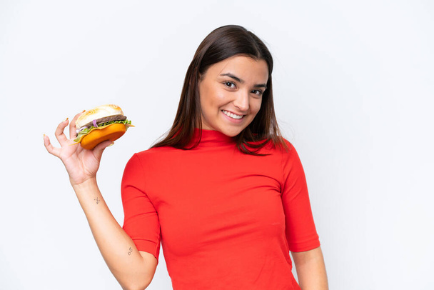Young caucasian woman holding a burger isolated on white background smiling a lot - Fotoğraf, Görsel