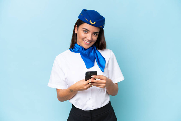 青い背景に隔離された飛行機スチュワーデス原因アジアの女性は、携帯電話でメッセージを送信します - 写真・画像