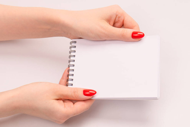 Un cuaderno con papel blanco vacío en manos de mujer con uñas rojas. Copiar espacio.  - Foto, Imagen