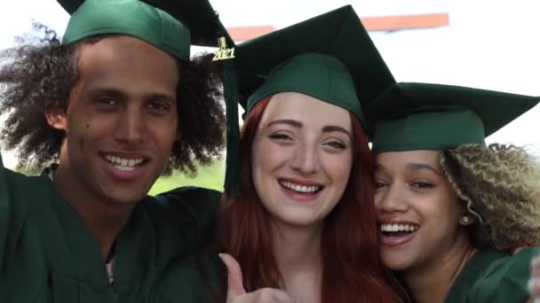 Heureux groupe d'étudiants le jour de la remise des diplômes, Trois meilleurs amis multiraciaux en robes académiques et casquettes célébrant devant la caméra - Séquence, vidéo