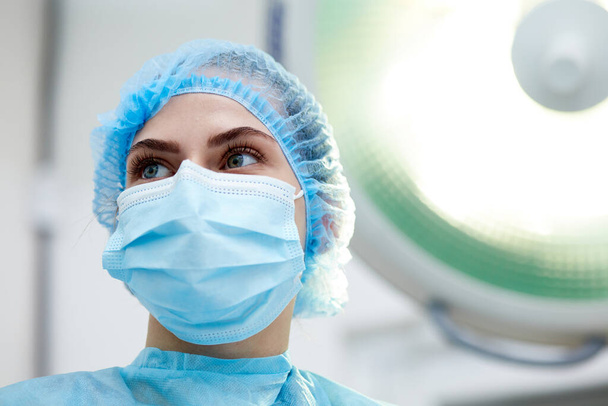 Close-up image of young woman, doctor, surgeon in protective medical mask leading surgery in medical clinic, hospital in surgery room. Concept of medicine, hospital, healthcare, treatment, profession - Foto, Imagem