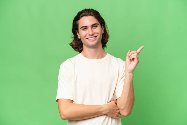 jovem caucasiano homem isolado no verde croma fundo feliz e apontando para cima - Foto, Imagem